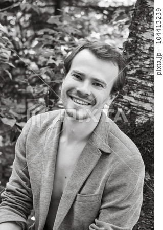 Black and white portrait of Self assured smiling young handsome man with naked chest and open grey jacket. Macho with dark hair, sideburns and beard looking at camera. Black and white portrait of Self assured smiling young handsome man with naked chest and open grey jacket. Macho with dark hair, sideburns and beard looking at camera. 104413239