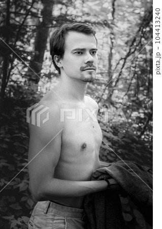 Black and white portrait handsome sexy man, athlete with perfect slender naked body standing three-quarters to the camera holding hand at neck, looking at camera in park. Man posing outdoors. High Black and white portrait handsome sexy man, athlete with perfect slender naked body standing three-quarters to the camera holding hand at neck, looking at camera in park. Man posing outdoors. High 104413240