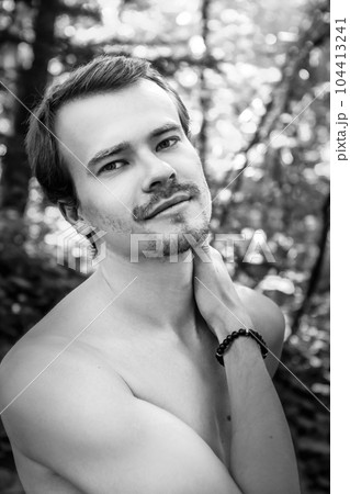 Black and white portrait handsome sexy man, athlete with perfect slender naked body standing three-quarters to the camera holding hand at neck, looking at camera in park. Man posing outdoors. High Black and white portrait handsome sexy man, athlete with perfect slender naked body standing three-quarters to the camera holding hand at neck, looking at camera in park. Man posing outdoors. High 104413241