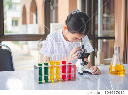 little scientist looking through a microscope and test tubes filled with chemicals for learning about science and experiments. 104417012
