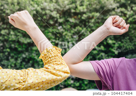 Cropped shot of two women bump elbows for greeting during coronavirus epidemic. Cropped shot of two women bump elbows for greeting during coronavirus epidemic. 104417404