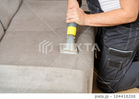 Dry cleaner's man employee removing dirt from textile furniture in flat. closeup, vacuum clean sofa Dry cleaner's man employee removing dirt from textile furniture in flat. closeup, vacuum clean sofa 104418208