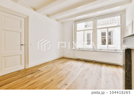 an empty living room with wood flooring and white paint on the walls there is a fireplace in the corner an empty living room with wood flooring and white paint on the walls there is a fireplace in the corner 104418265