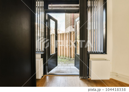an empty room with wooden floors and black doors that lead into the entrance to the yard, where there is no one in sight an empty room with wooden floors and black doors that lead into the entrance to the yard, where there is no one in sight 104418338