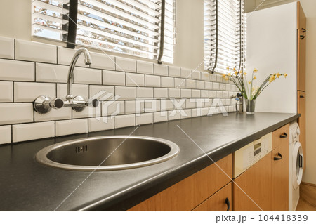 a kitchen with black counter tops and white tiles on the wall behind it is a sink in front of a window a kitchen with black counter tops and white tiles on the wall behind it is a sink in front of a window 104418339