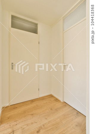 an empty room with white walls and wood flooring the door is open on the right side of the room 104418368