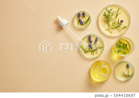 Petri dishes in many sizes are arranged with beaker, flask and a dropper on pastel background. Product extracted from Lavender (Lavandula) can be displayed in the left size  104418697
