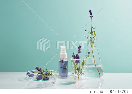 Mini pump bottle of purple liquid standing on podium in round shape. Glassware arranged over blue background. Skincare concept of Lavender (Lavandula) extract with empty label  104418707