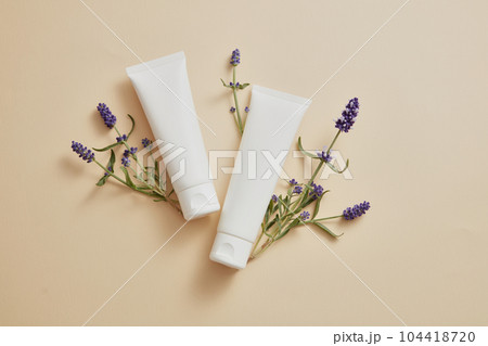 Over beige background, two white tubes are displayed with lavender flower. Mockup of skin care cosmetic tube of beauty facial extracted from Lavender (Lavandula) 104418720