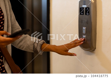 Midsection of biracial casual businesswoman using smartphone and calling elevator in office 104418775