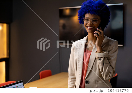 Portrait of happy biracial casual businesswoman with blue afro talking on smartphone in office Portrait of happy biracial casual businesswoman with blue afro talking on smartphone in office 104418776