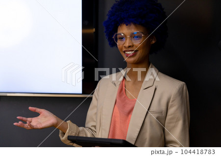 Happy biracial casual businesswoman with blue afro making presentation at whiteboard with copy space 104418783