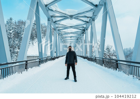 man tourist Visiting in Biei, Traveler in Sweater sightseeing Shirahige Waterfall bridge with Snow in winter. landmark and popular for attractions in Hokkaido, Japan. Travel and Vacation concept 104419212