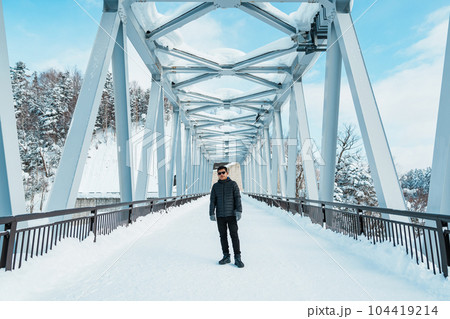 man tourist Visiting in Biei, Traveler in Sweater sightseeing Shirahige Waterfall bridge with Snow in winter. landmark and popular for attractions in Hokkaido, Japan. Travel and Vacation concept 104419214