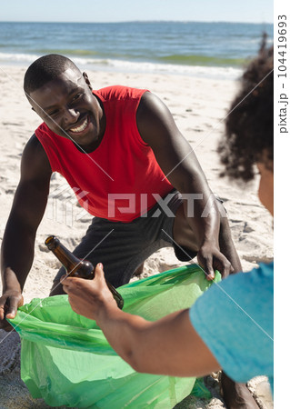 Happy african american couple cleaning sunny beach and collecting litter 104419693