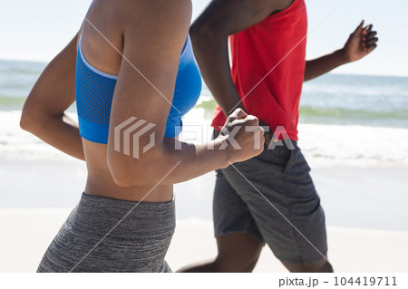 Midsection of fit african american couple exercising, running on sunny beach 104419711