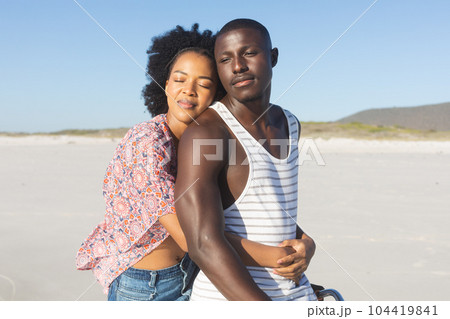 Happy african american couple embracing and smiling with eyes closed on sunny beach 104419841