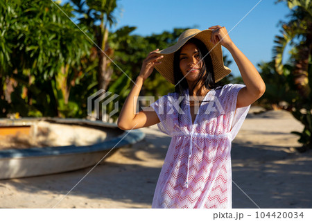 Portrait of happy biracial woman in white beach dress and sunhat smiling on sunny beach Portrait of happy biracial woman in white beach dress and sunhat smiling on sunny beach 104420034