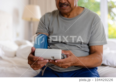 Mid section of biracial senior man taking blood pressure in bed at home Mid section of biracial senior man taking blood pressure in bed at home 104420226