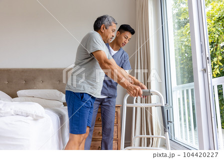 Diverse male doctor advising and senior male patient using crutches at home 104420227