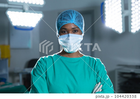 Portrait of african american female surgeon wearing surgical gown and face mask in operating theatre 104420338