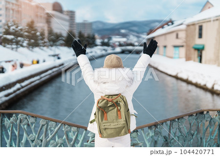 Woman tourist Visiting in Otaru, happy Traveler in Sweater sightseeing Otaru canal with Snow in winter season. landmark and popular for attractions in Hokkaido, Japan. Travel and Vacation concept 104420771