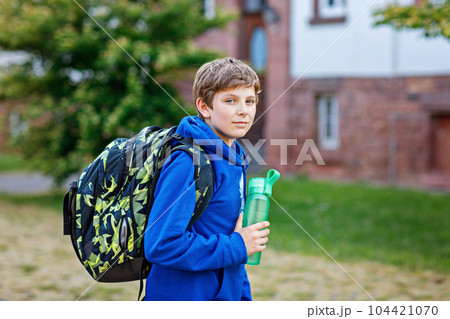 Happy preteen kid boy with backpack or satchel and water bottle. Schoolkid in on the way to elementary or middle school on warm sunny summer day. Healthy child outdoors on the street in the city 104421070