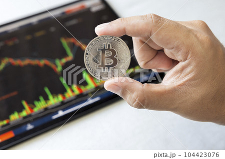 Close-up hand of man holding crypto coin on chart in tablet background. Blockchain technology finance future. Male hold bitcoin. concept about business, finance, trade, economy, banking, investment. 104423076