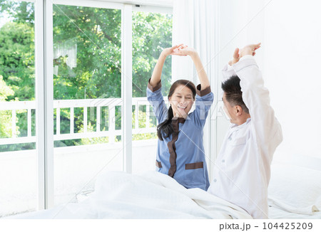 朝ベッドでストレッチする笑顔の高齢者夫婦 104425209