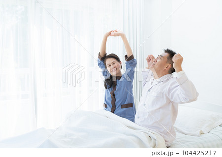 朝ベッドでストレッチする笑顔の高齢者夫婦 104425217