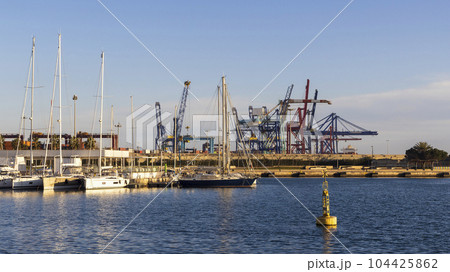 Spain, Valencia, Sailboats moored at marina with dock cranes in background 104425862