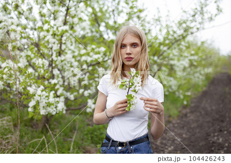 Portrait of woman holding branch of apple tree in orchard 104426243