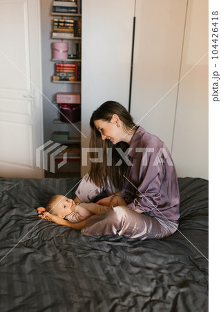 Happy mother holds a baby baby in her arms, smiling, sitting on the bed Happy mother holds a baby baby in her arms, smiling, sitting on the bed 104426418