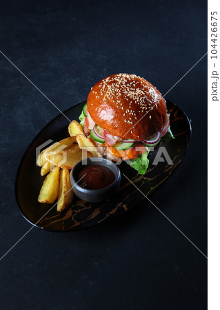 Burger with beef patty. Marbled meat.Served with potato slices. Black background.Copy space. Vertical photo. 104426675