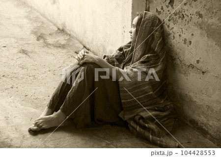 A girl in poor clothes sits on the ground 104428553