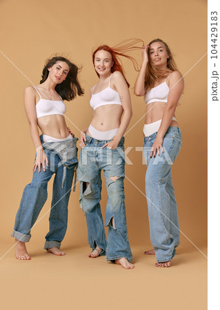 Delightful look. Full-length portrait of beautiful young women in underwear top and jeans posing against studio background 104429183