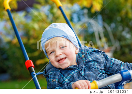 Cute little boy playing with tricycle bike outdoors. Happy child play in autumn park. Toddler baby boy wears trendy jacket. smiling Blonde boy portrait. Autumn fashion. Stylish child outside. Cute little boy playing with tricycle bike outdoors. Happy child play in autumn park. Toddler baby boy wears trendy jacket. smiling Blonde boy portrait. Autumn fashion. Stylish child outside. 104431054