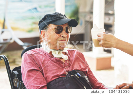 Senior man of 85 years in an electric wheelchair is sitting in a park. Nurse supporting man with drinking coffee, holding cup. Senior man of 85 years in an electric wheelchair is sitting in a park. Nurse supporting man with drinking coffee, holding cup. 104431056