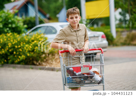 onfident School Boy Pushes the Shopping Cart Through a Bustling Supermarket. Handsome Teenager Gathers Groceries and Navigates the Aisles Independently, Showcasing Responsibility and Maturity 104431123