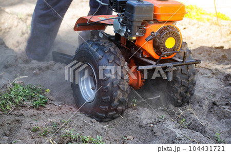 Plowing a garden with potatoes with a walk-behind tractor. Harvesting potatoes in autumn. Plowing the furrow with a motor-block with a plow. Industry 104431721