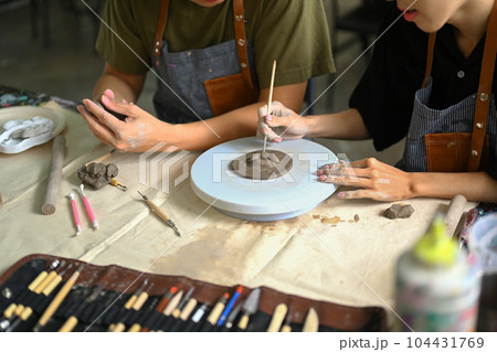 Cropped shot of man sculpting clay plate on pottery wheel, creating handmade ceramics in art class 104431769