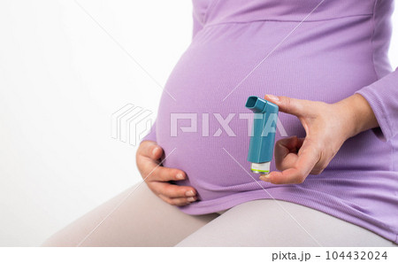Pregnant girl with an inhaler in her hand on the background of her stomach. The concept of exacerbation of asthma in pregnant women. Copy space for text 104432024