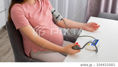A pregnant girl measures blood pressure with a device. The concept of high and low blood pressure during pregnancy. Arterial hypertension. Copy space for text A pregnant girl measures blood pressure with a device. The concept of high and low blood pressure during pregnancy. Arterial hypertension. Copy space for text 104432081