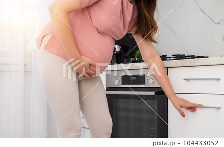 pregnant girl in a modern kitchen. The concept of heaviness and discomfort when cooking with a large belly in the last trimester. pregnant girl in a modern kitchen. The concept of heaviness and discomfort when cooking with a large belly in the last trimester. 104433052