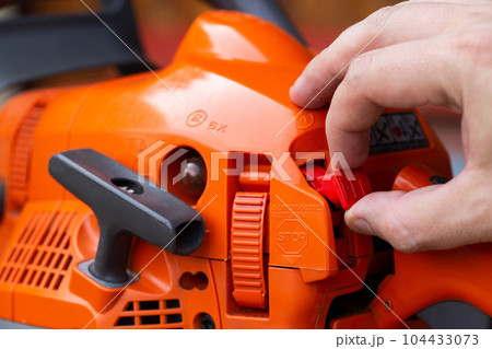 Opening and closing the throttle by moving the combination lever up one detent position to start the chainsaw engine. Close-up, industry Opening and closing the throttle by moving the combination lever up one detent position to start the chainsaw engine. Close-up, industry 104433073