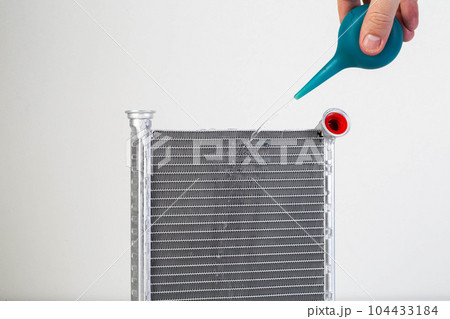 A jet of water from a syringe pours onto a car radiator. The concept of cleaning and flushing car radiators from pollution. Clogged radiator cells. Copy space for text A jet of water from a syringe pours onto a car radiator. The concept of cleaning and flushing car radiators from pollution. Clogged radiator cells. Copy space for text 104433184