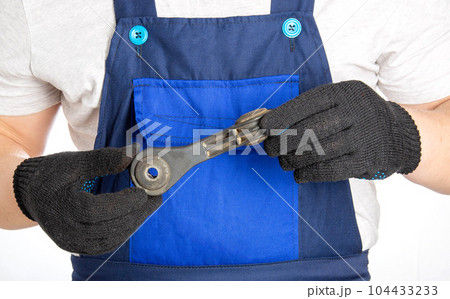 A car mechanic holds in his hands a part of a car suspension, a stabilizer link. Repair and replacement of car auto parts at a car service, close-up 104433233