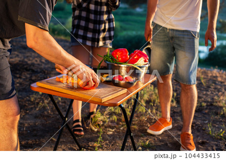 A man cuts vegetables on a salad table. Outdoor recreation in summer with friends. Cooking, close-up A man cuts vegetables on a salad table. Outdoor recreation in summer with friends. Cooking, close-up 104433415