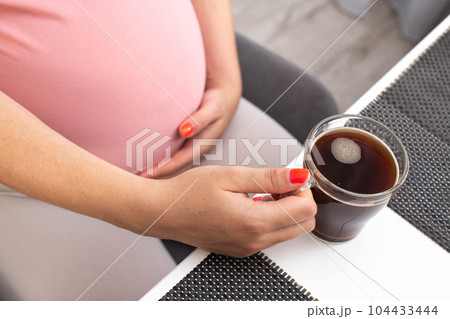 Big belly of a pregnant girl and a cup of coffee in her hand. The benefits and harms of coffee for pregnant women. Big belly of a pregnant girl and a cup of coffee in her hand. The benefits and harms of coffee for pregnant women. 104433444