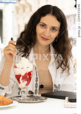 Young woman eating strawberry ice cream while sitting in an outdoor cafe 104433846